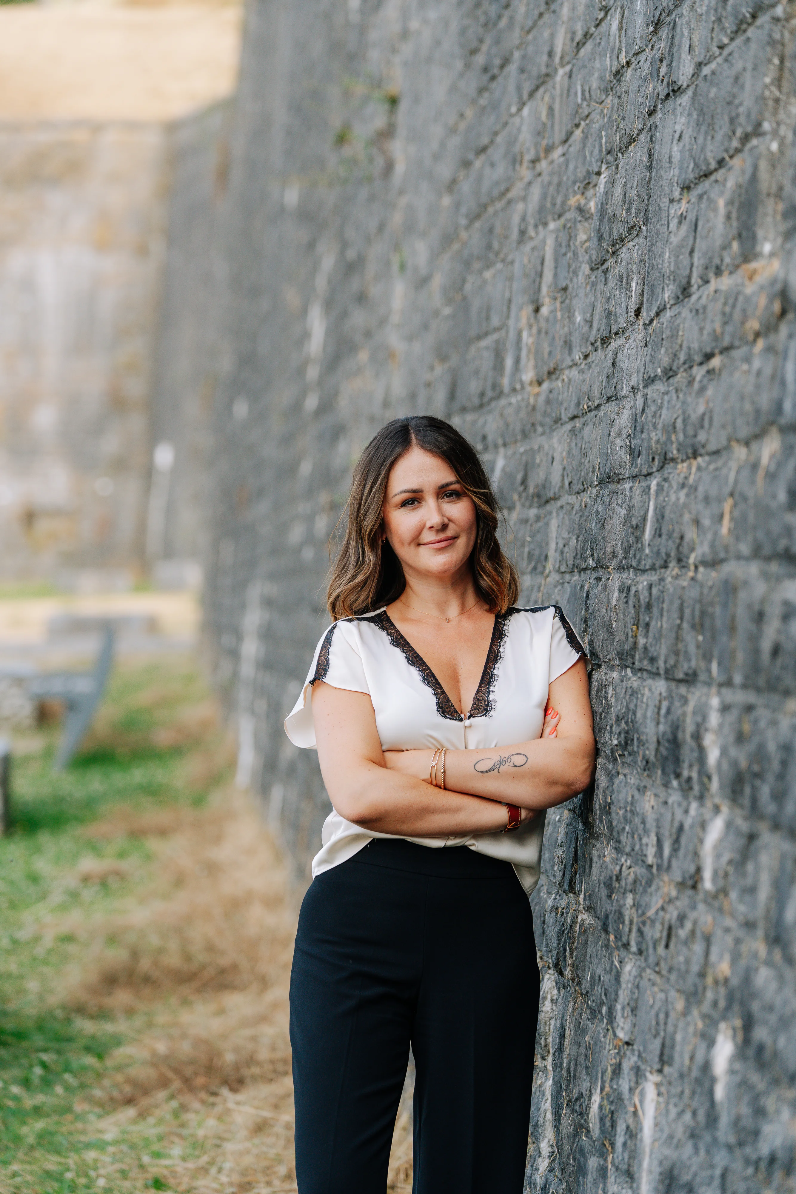 Photo de Justine Dubail souriante tenant un panneau À VENDRE de son entreprise Dubail Immobilier, prise en extérieur avec vue sur la vallée de Namur.
